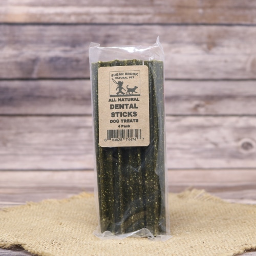 A pack of Sugar Brook all-natural Dental Sticks dog treats, vertically aligned and encased in clear packaging, on a burlap mat against a wooden backdrop.
