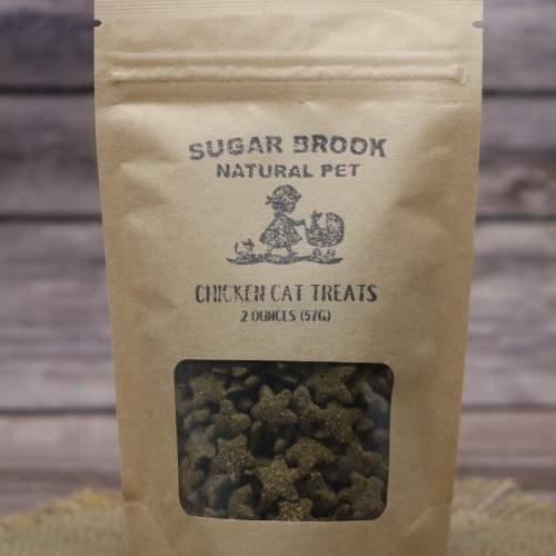 Close-up of Sugar Brook Natural Pet Chicken Cat Treats in a kraft paper pouch with a window, against a burlap and wooden background