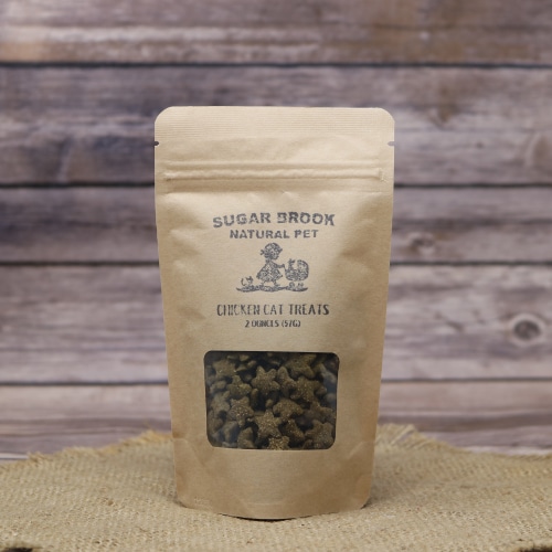 A stand-up pouch of Sugar Brook Natural Pet Chicken Cat Treats on a woven burlap mat with a rustic wooden background.
