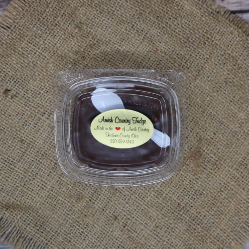 Clear plastic Ashery bowl with yellow sticker label on the plastic lid, filled with chocolate fudge, sitting on a burlap material with wood background