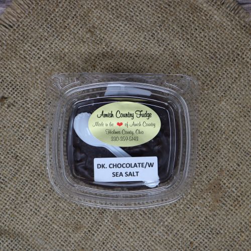 Clear plastic Ashery bowl with yellow sticker label on the plastic lid, filled with dark chocolate fudge, sitting on a burlap material with wood background