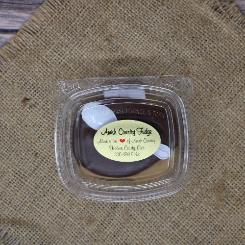 Clear plastic Ashery bowl with yellow sticker label on the plastic lid, filled with peanut butter fudge, sitting on a burlap material with wood background