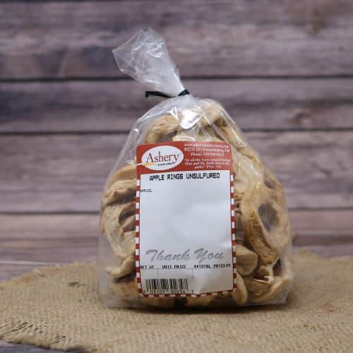Clear plastic Ashery bag with red and white sticker label filled with dried apple rings, sitting on a burlap material with wood background