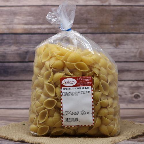 Clear plastic Ashery bag with red and white sticker label filled with Conchiglie Rigati shells, sitting on a burlap material with wood background