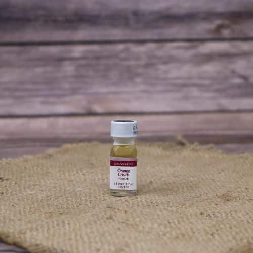 small clear bottle with a red and white label and a sealed lid, with a clear tan liquid in it, sitting on a burlap material with wood background