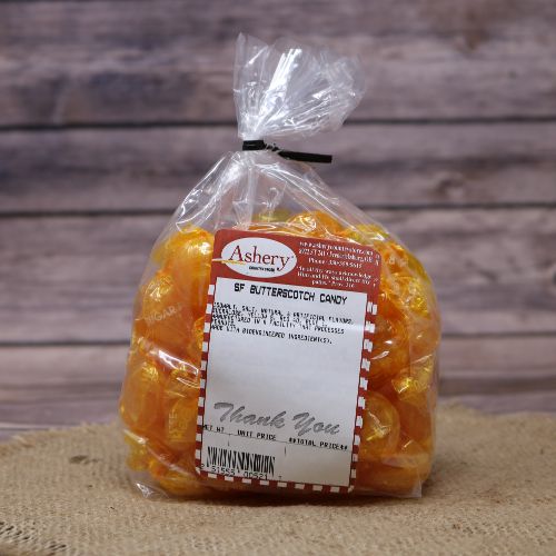 Clear plastic Ashery bag with red and white sticker label filled with orange butterscotch candies, sitting on a burlap material with wood background