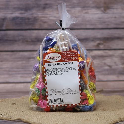 Clear plastic Ashery bag with red and white sticker label filled with assorted tootsie roll pops, sitting on a burlap material with wood background