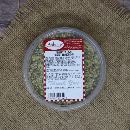 Container of Ashery's Own Pesto Seasoning blend viewed from above, set on a woven burlap mat with a wooden background.