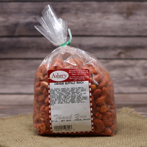 Bag of Ashery's Buffalo Ranch Cashews, with a reddish tint to the nuts, secured with a twist tie on a straw mat and wooden background.