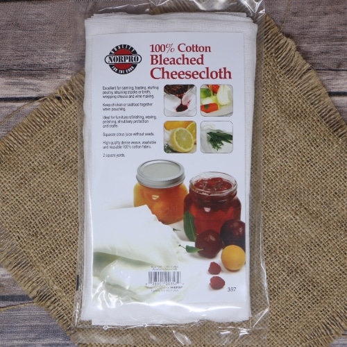 Pack of Norpro 100% cotton bleached cheesecloth on a straw mat, with a wooden background and images of its uses on the packaging.