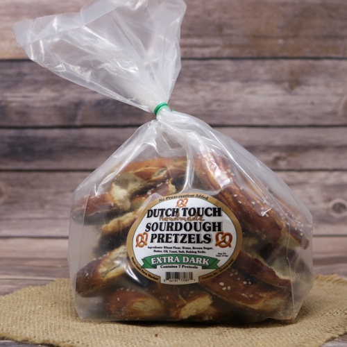A bag of Dutch Touch extra dark sourdough pretzels on a natural straw mat, with a warm wooden background.