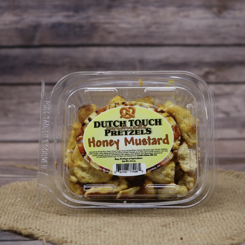 A clear container of Dutch Touch Honey Mustard Pretzels on a hessian burlap mat, with a wooden background giving a homely feel.