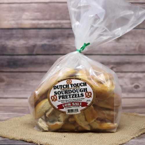 Bag of Dutch Touch low-salt sourdough pretzels tied with a twist, displayed on a textured straw mat and wood grain background.