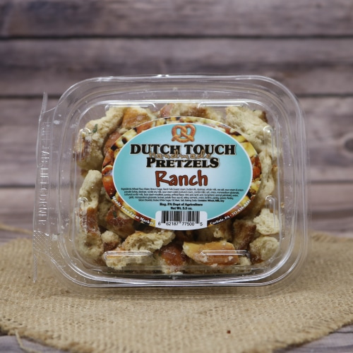 Dutch Touch Ranch Pretzels in a see-through container placed on a burlap mat, with a wood grain pattern in the background.