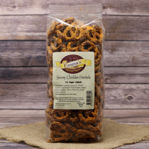 Packaged Emma's Savory Cheddar Pretzels in a clear plastic bag placed on a woven mat with a wooden plank backdrop.