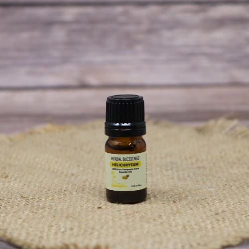 Bottle of Herbal Blessings Helichrysum essential oil on a burlap mat with a rustic wooden background.