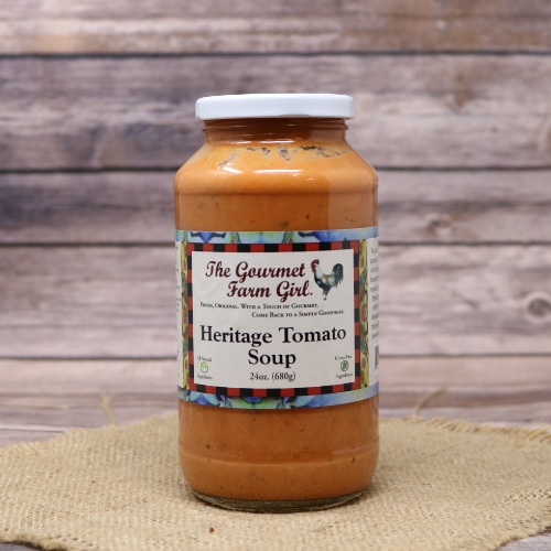 Jar of The Gourmet Farm Girl Heritage Tomato Soup on a straw mat, with the warm tones of the soup complemented by the wooden background.