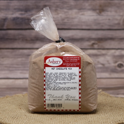 A bag of Ashery's hot chocolate mix secured with a twist tie, set on a woven straw mat against a rustic wood background."