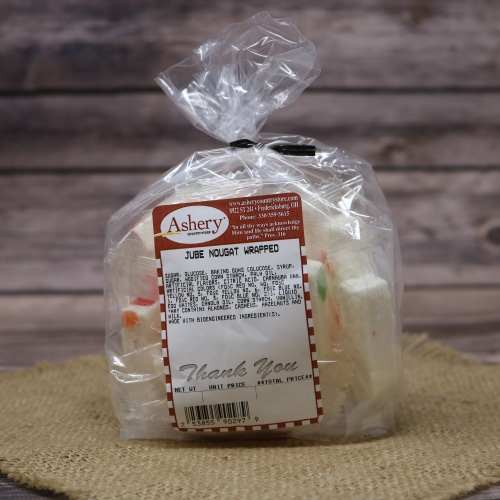 Clear plastic bag of Ashery Jube Nougat Wrapped candies sitting on a woven mat, with a rustic wood panel backdrop.