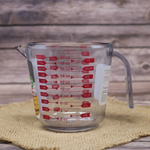 Clear measuring cup with red measurement markings on a burlap mat with a rustic wooden background.