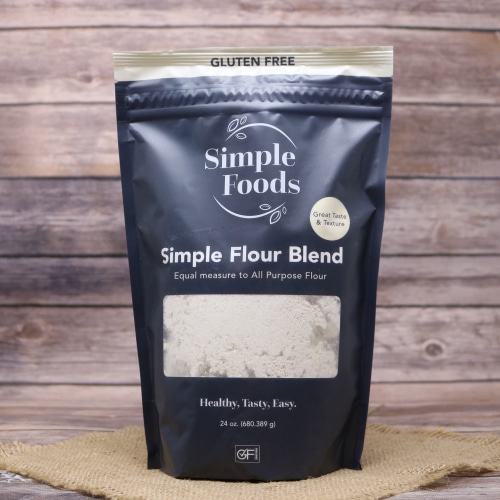 A stand-up pouch of Simple Foods Simple Flour Blend, labeled gluten-free, on a natural straw mat with a wood-patterned backdrop.