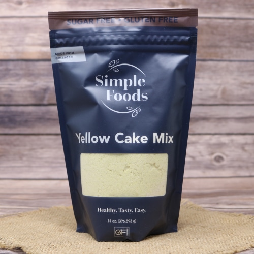 Bag of Simple Foods Yellow Cake Mix on a burlap mat with a rustic wooden background.