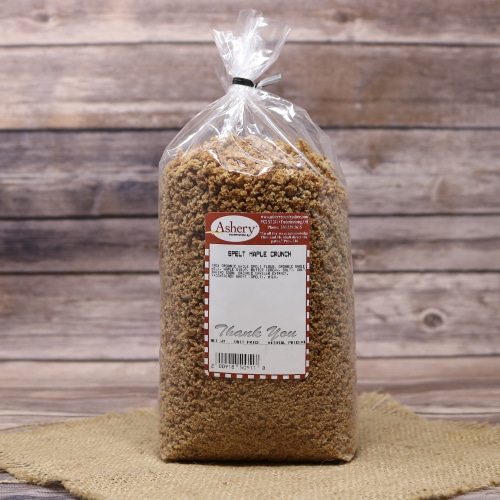 A bag of Stutzman Farms Spelt Maple Crunch on a natural straw mat, against a rustic wooden background.