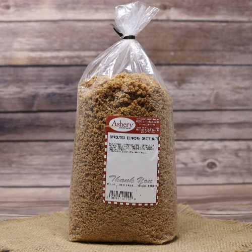 A clear plastic bag of Stutzman Farms Sprouted Einkorn Grate Nuts on a straw mat, with a vintage wood background.