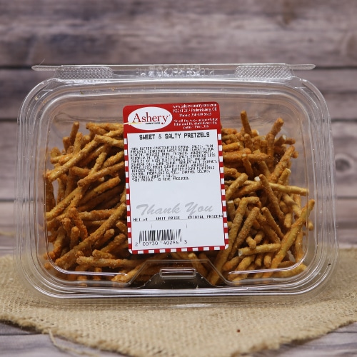 A transparent container of Ashery Sweet & Salty Pretzels on a burlap mat, with a subtle wooden background enhancing the treat's appeal.